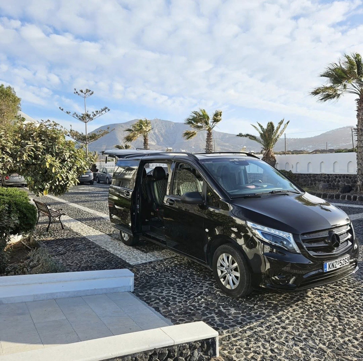 Black Mercedes-Benz Vito Tourer with its door open, overlooking the caldera